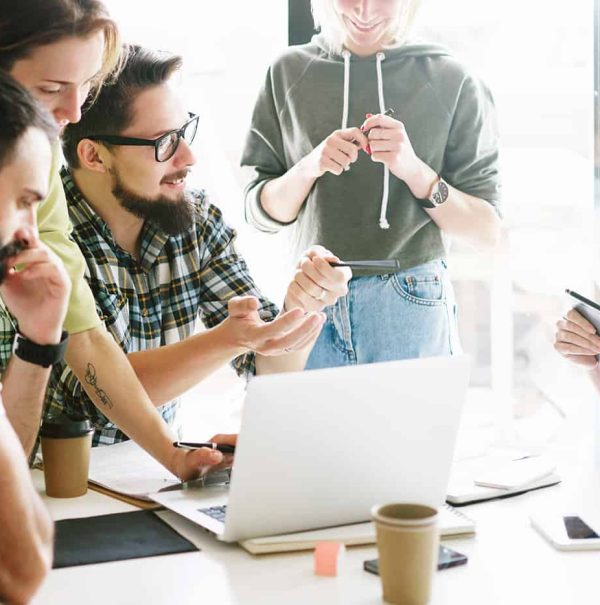 A group of old friends sitting around a table at home, looking at a laptop.
